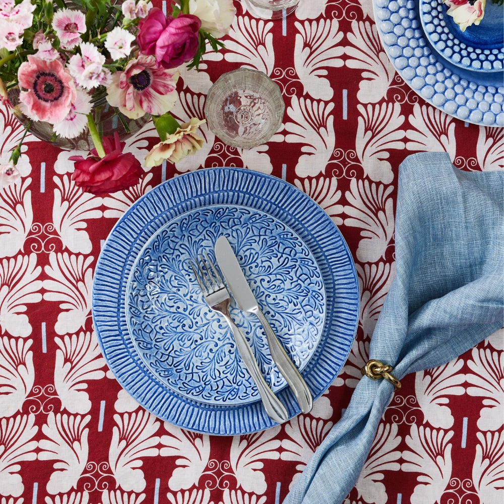 Blue ceramic plate with floral design on a red and white patterned tablecloth with flowers and cutlery.