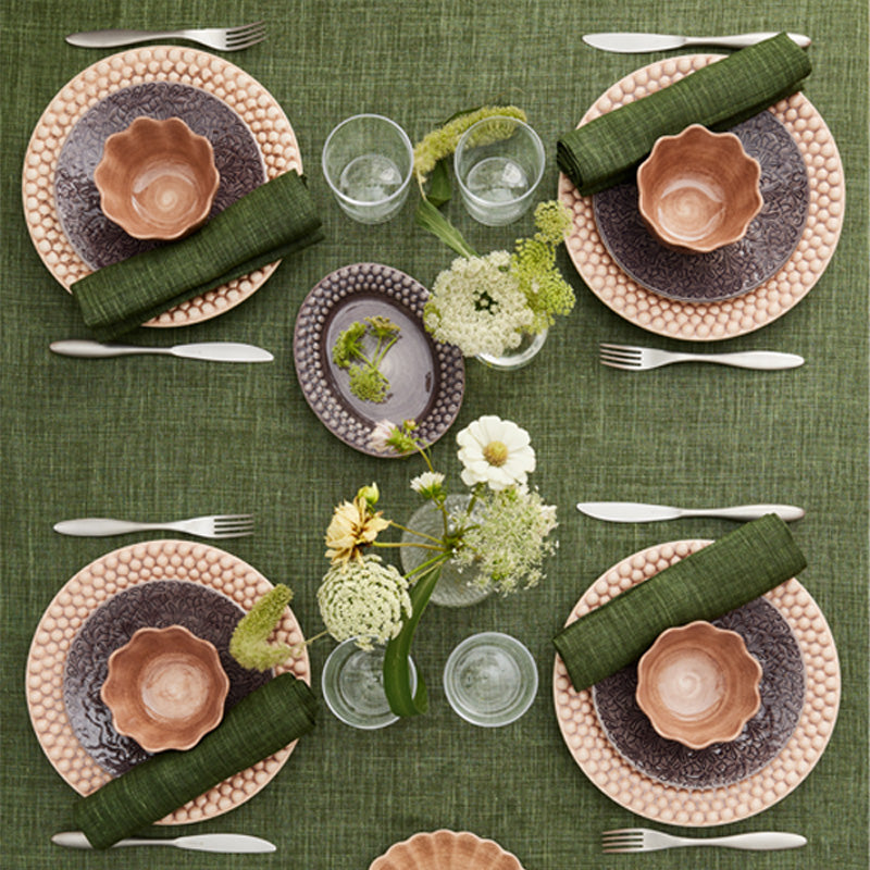 Set dining table with ceramic plates, cutlery, and floral arrangements on a green textured tablecloth.