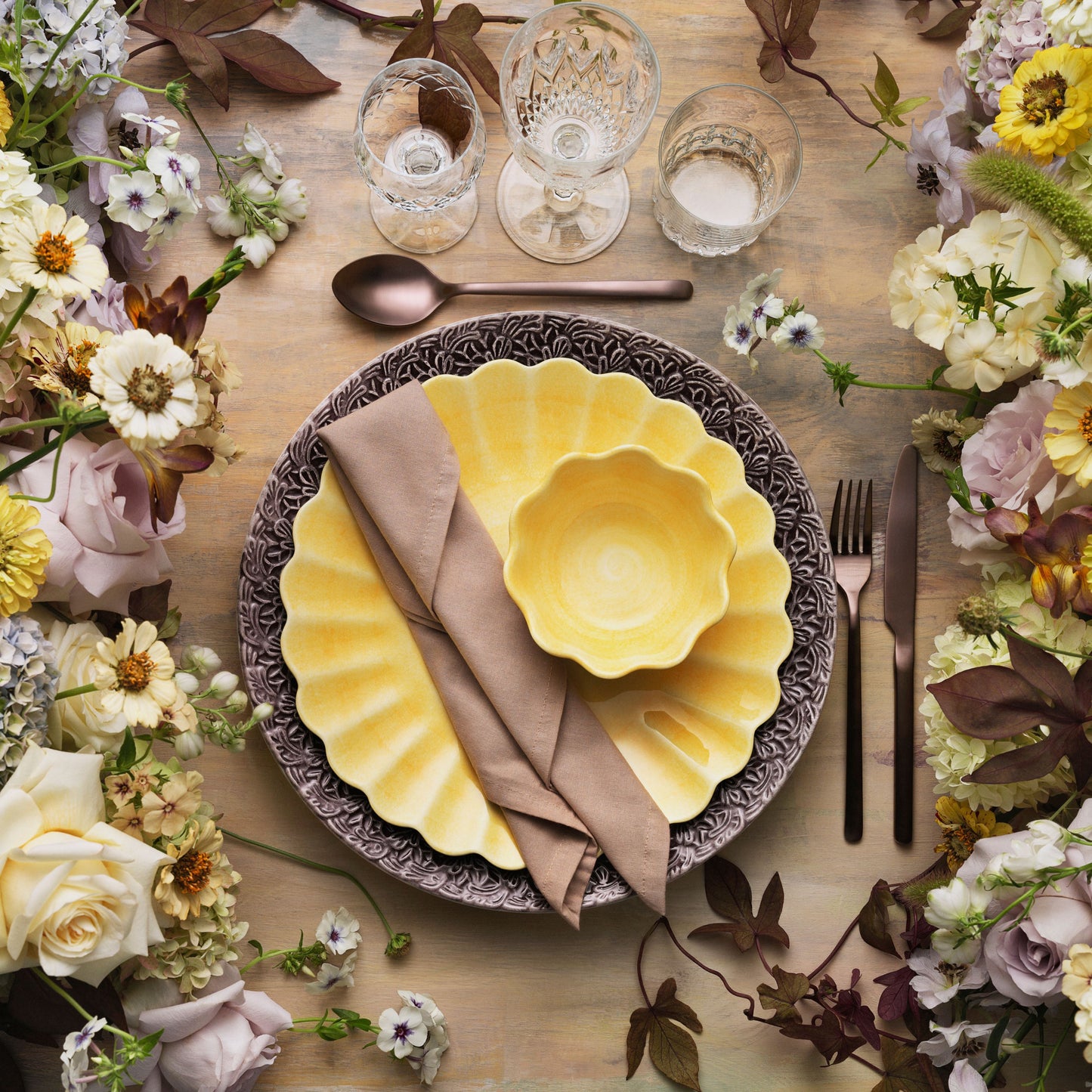 Elegant table setting with yellow plates, silverware, and floral decorations.