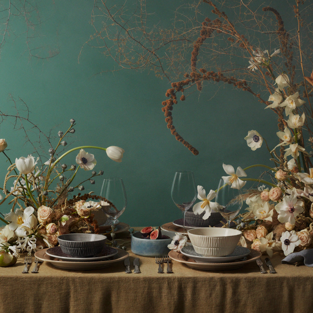 Decorative table setting with flowers, bowls, and wine glasses against a green wall.