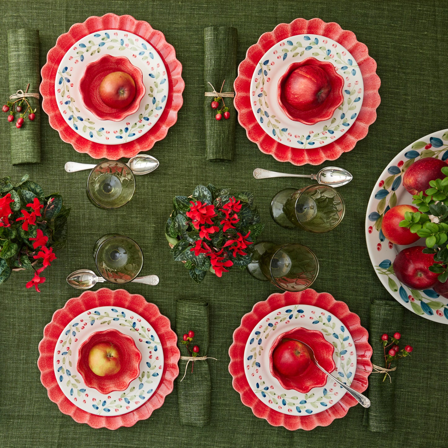 Set of ceramic plates with red fruit design on a green tablecloth.