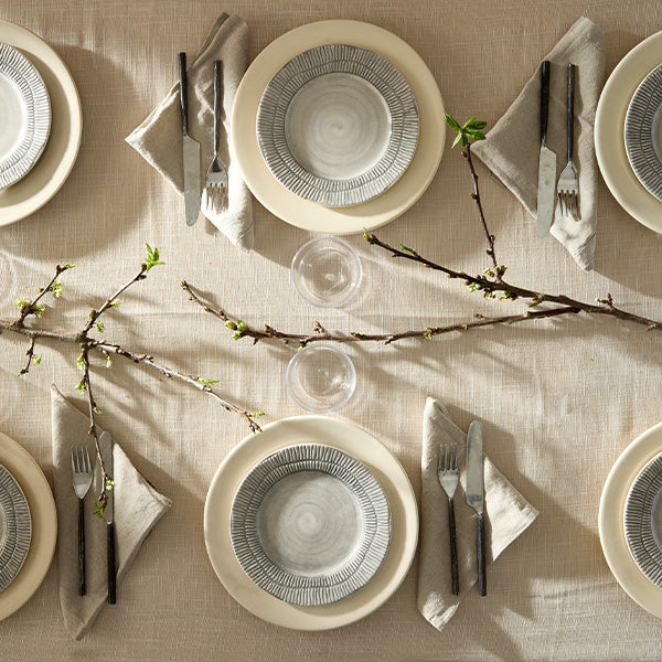 Elegant table setting with beige plates, silverware, and green branches on a beige tablecloth.