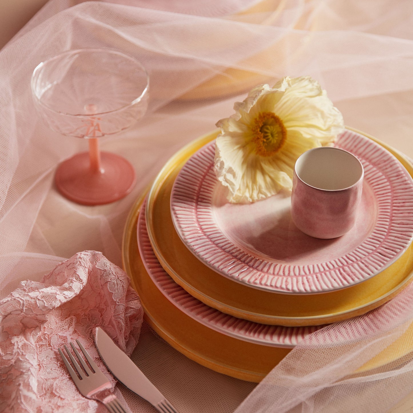 Pink and yellow ceramic plates with a flower and glass on a soft pink background