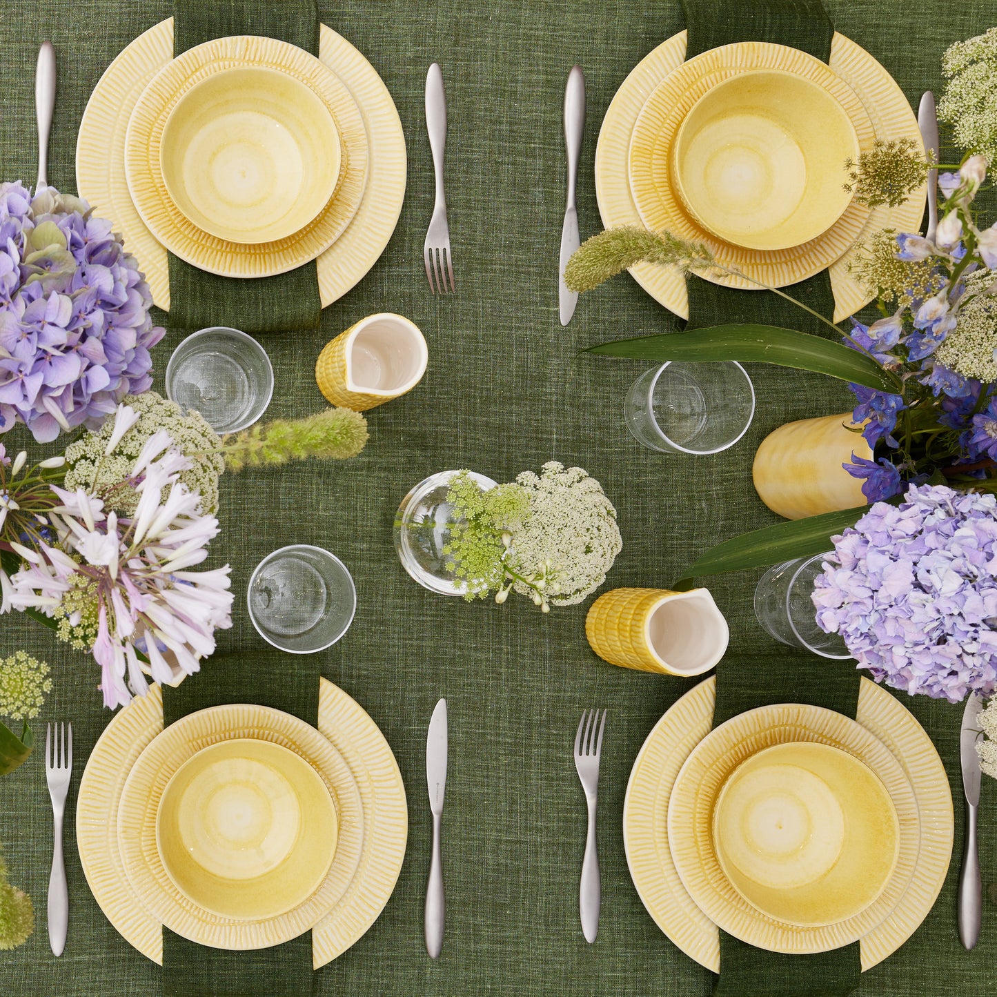 Elegant table setting with yellow plates, silverware, and purple flowers on a green tablecloth.
