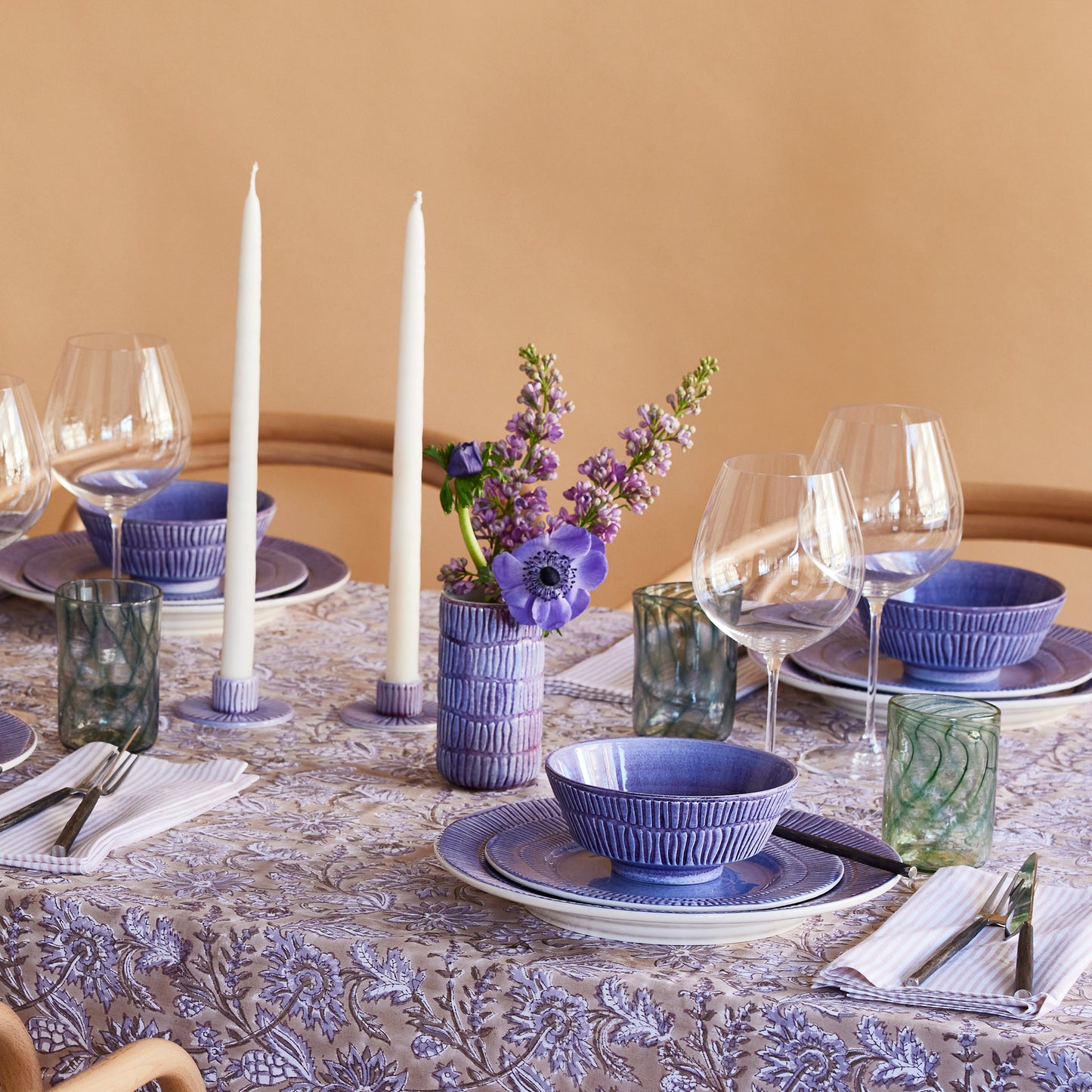 Dining table set with blue and white dishes, candles, and a vase with flowers on a beige background.
