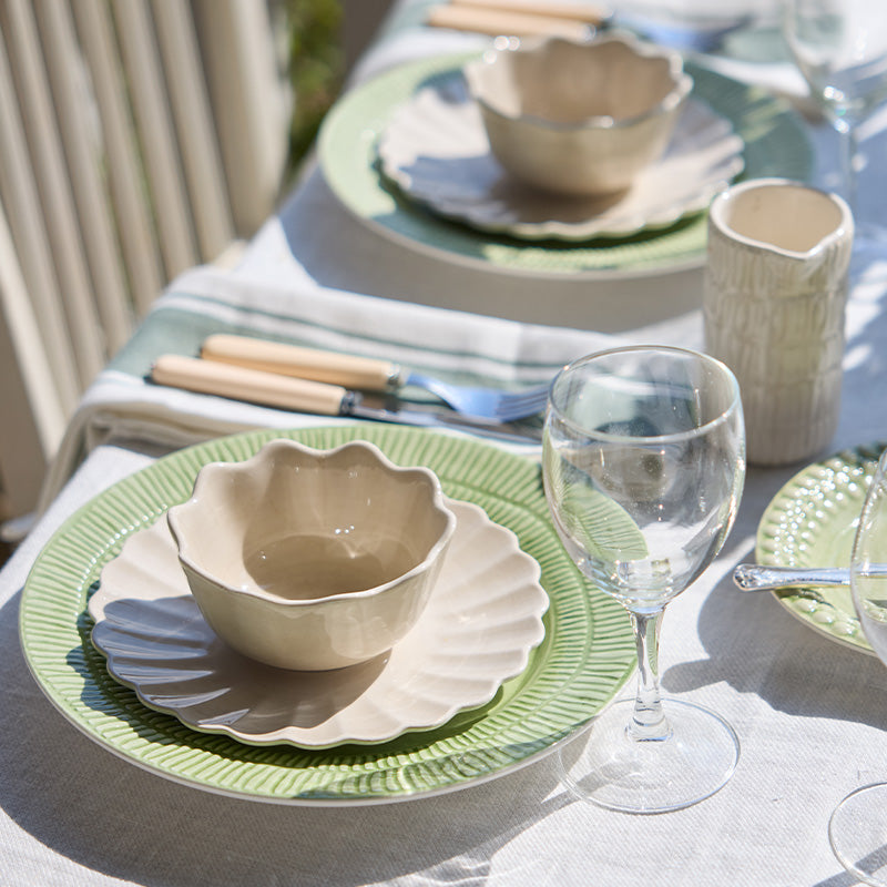 Dining table setting with ceramic bowls, plates, and a glass on a light surface.