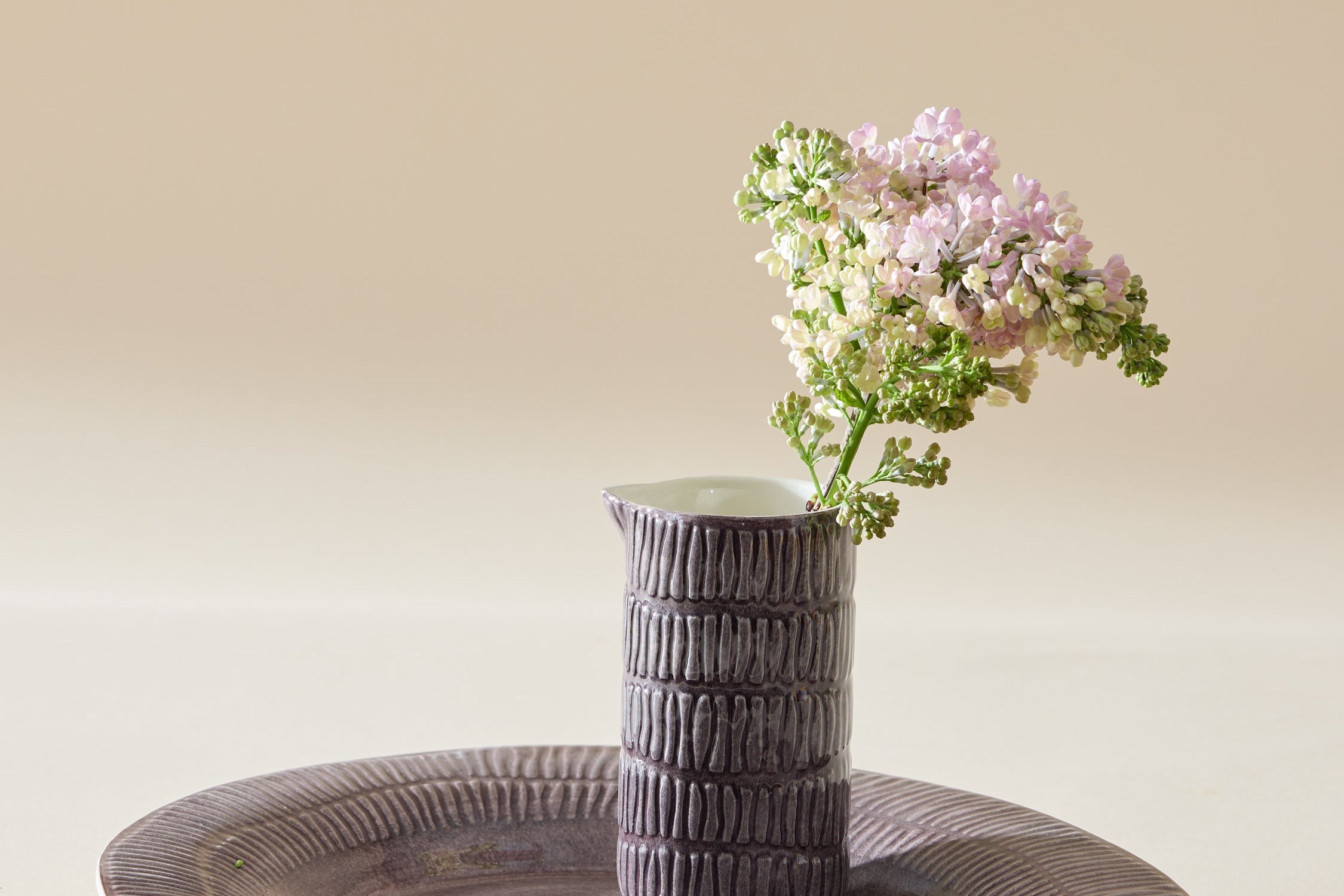 Ceramic vase with flowers on a matching plate against a beige background