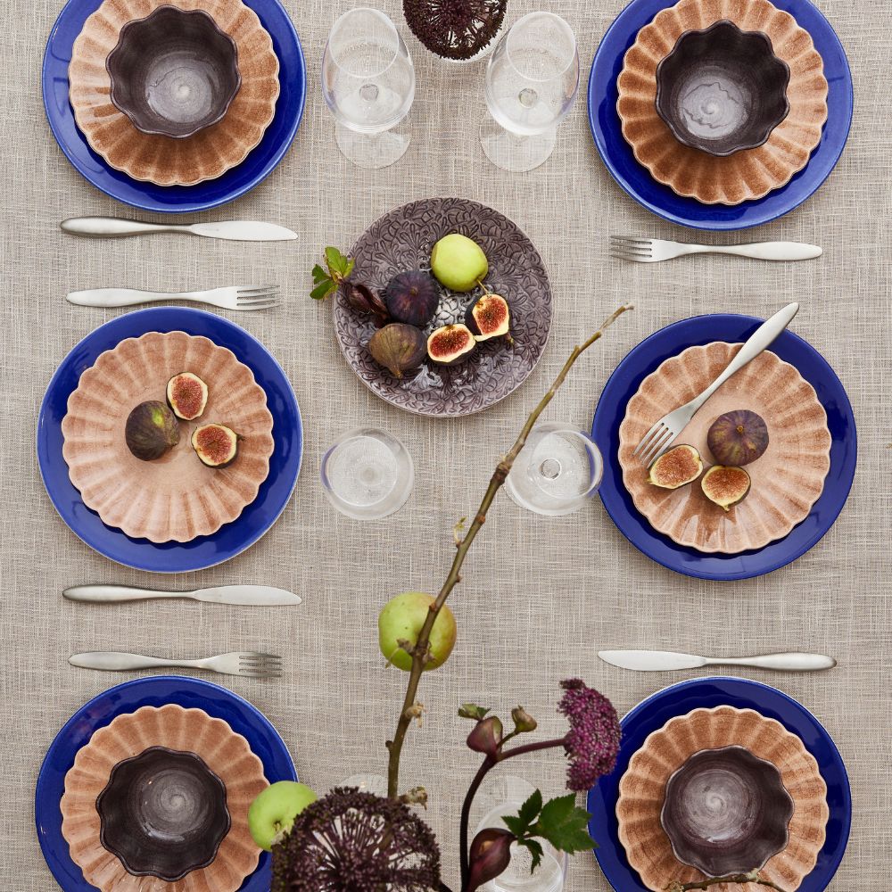 Dinner table setting with plates, glasses, and cutlery on a textured tablecloth.