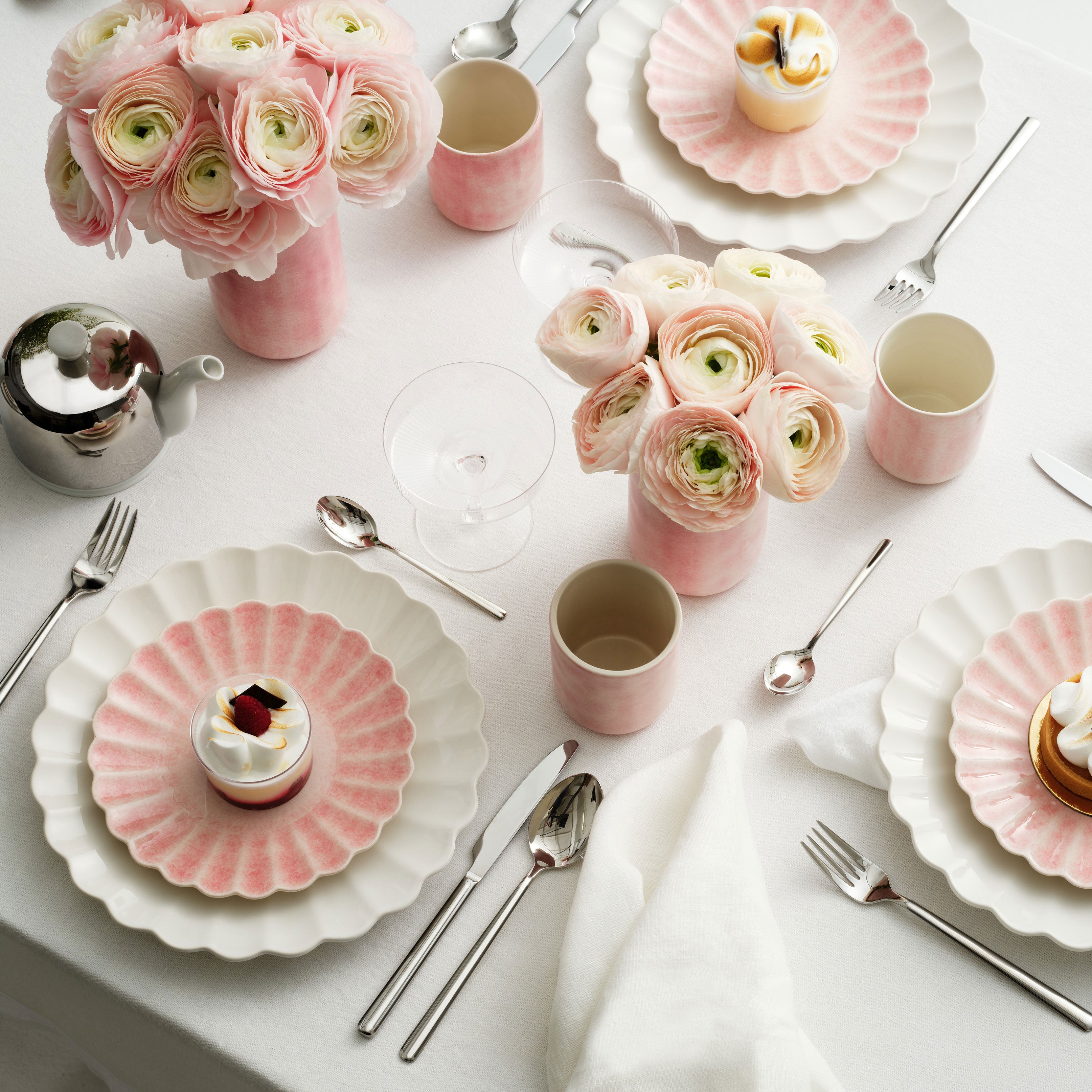 Elegant table setting with pink and white floral arrangements, plates, and silverware on a white tablecloth.