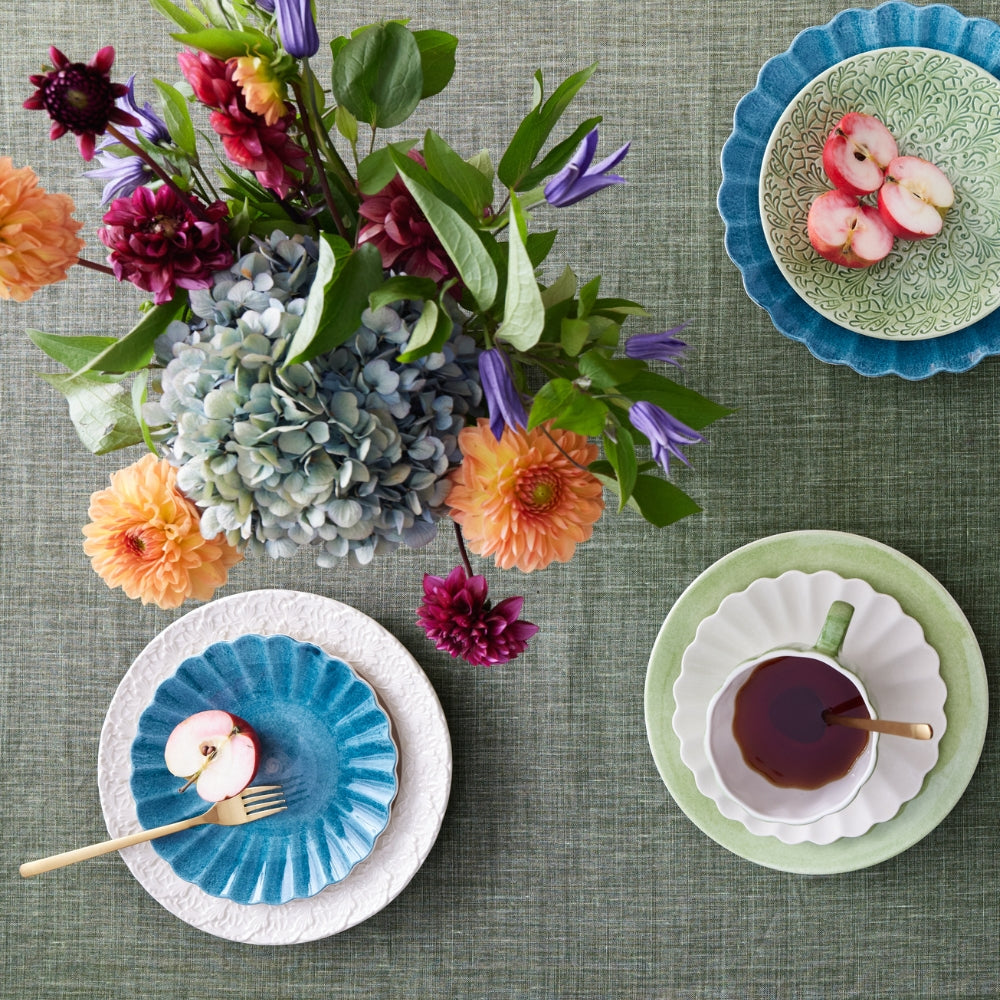 Table setting with floral arrangement, plates, and a cup on a green tablecloth.