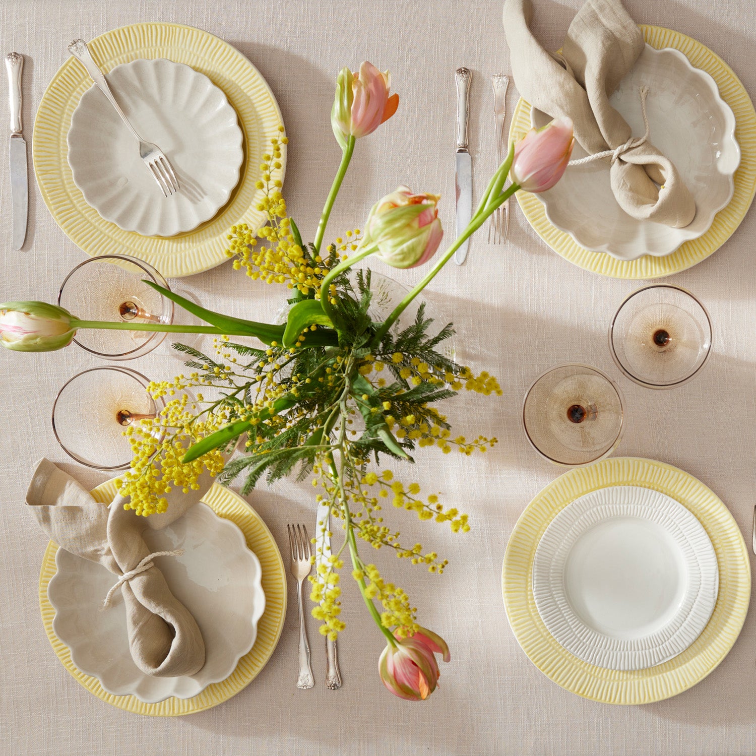 Elegant table setting with yellow and white plates, glasses, and a floral centerpiece.
