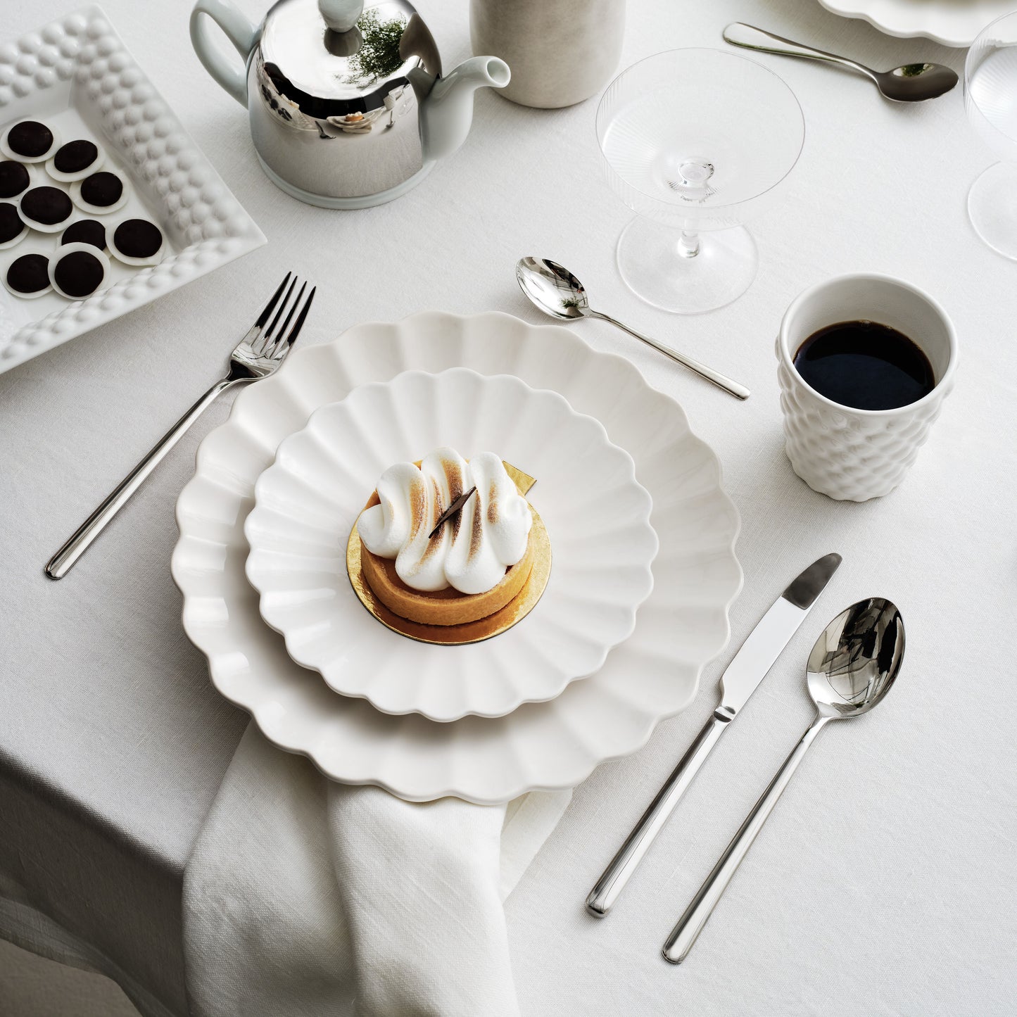 Table setting with a dessert, coffee, and cutlery on a white tablecloth.