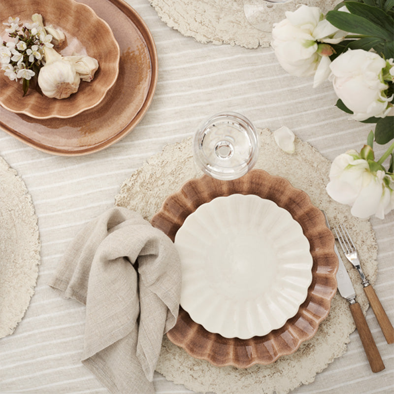 Elegant table setting with ceramic plates, glass, cutlery, and flowers on a textured surface.