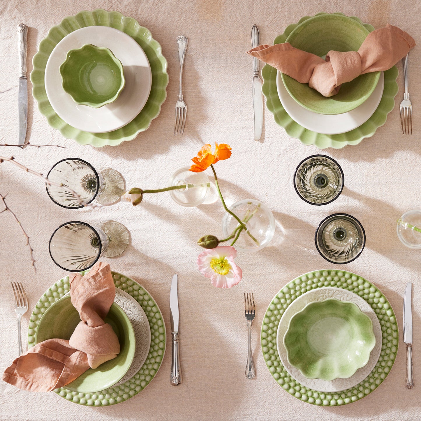 Elegant table setting with green plates, pink napkins, and floral decorations on a light background.