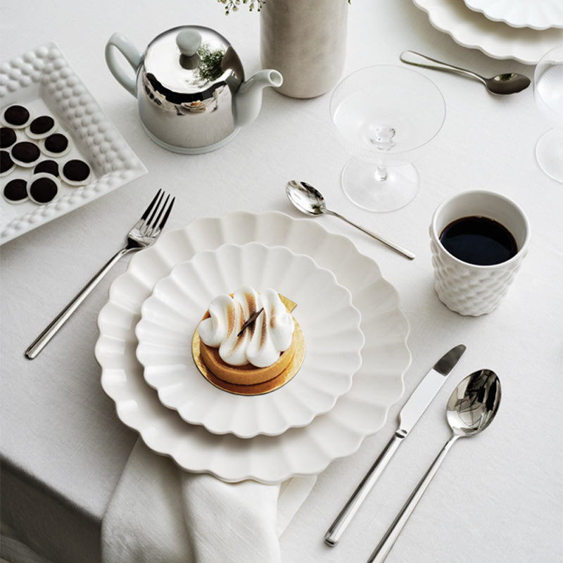 Table setting with a dessert, coffee, and utensils on a white tablecloth.