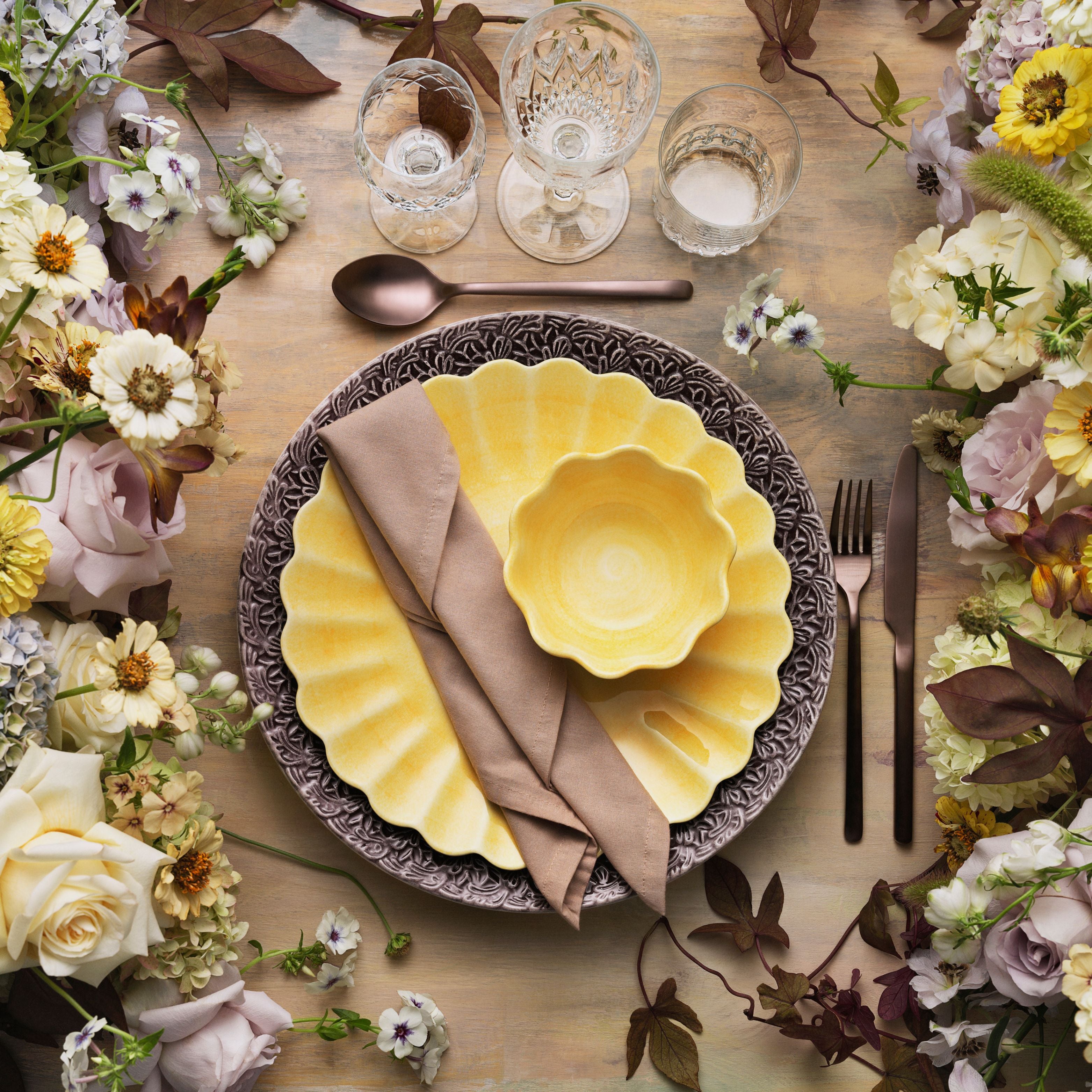 Elegant table setting with yellow plates, silverware, and floral decorations.