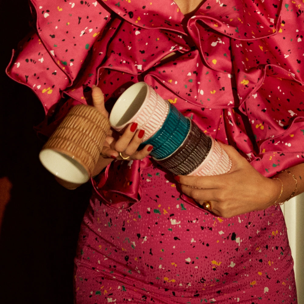 Person holding five patterned cups against a pink dress