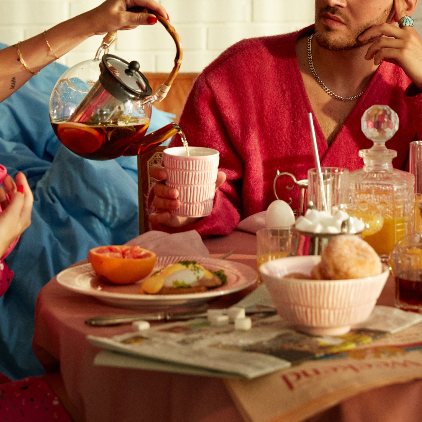 Person pouring tea into a cup at a table with food and drinks.