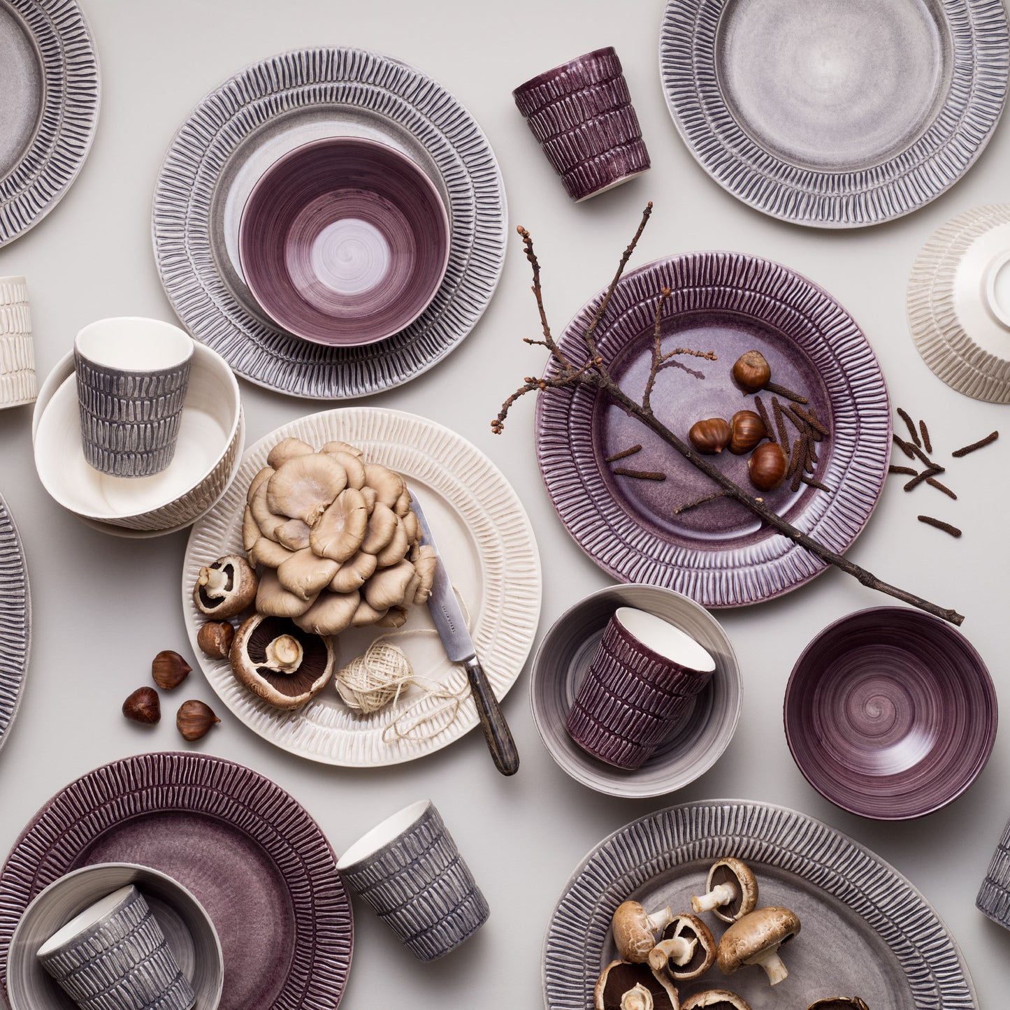 Table setting with purple and gray ceramic plates, bowls, and mugs on a light background.