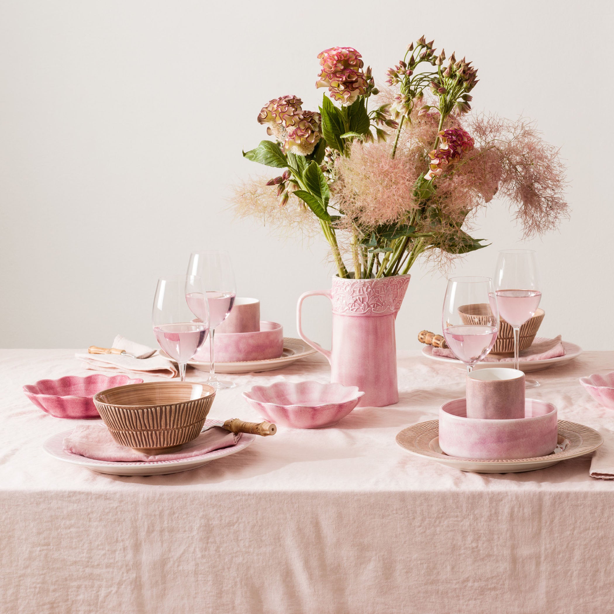 Dining table set with pink ceramic dishes and a vase of flowers on a light background