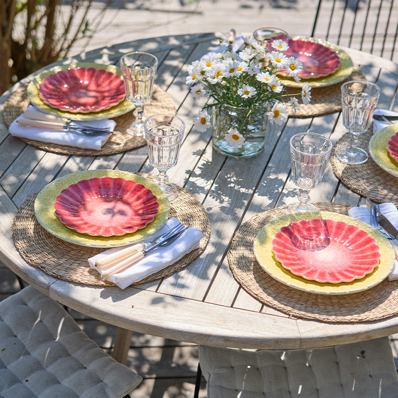 Outdoor table setting with colorful plates, glasses, and flowers on a wooden table.