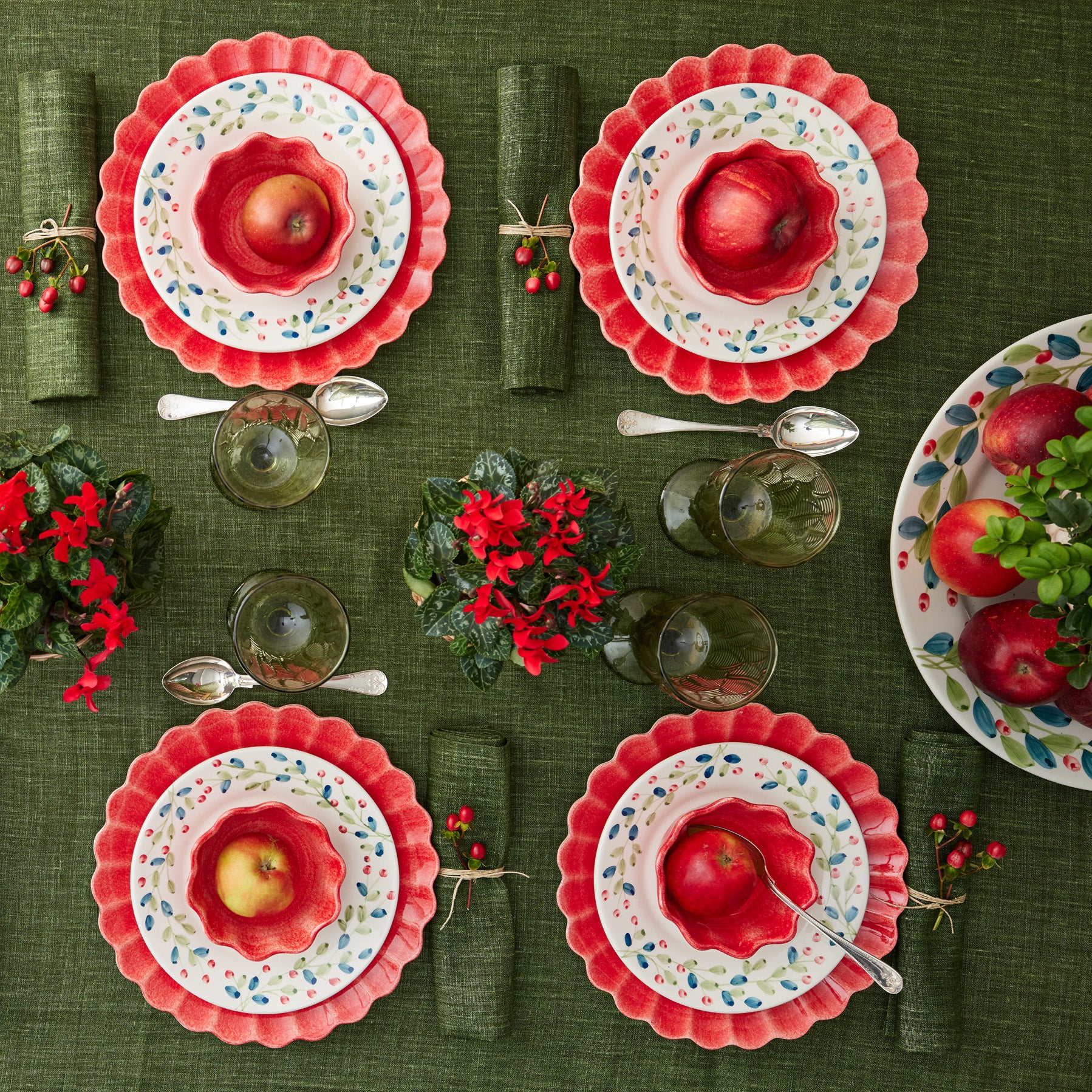 Set of ceramic plates with red fruit design on a green tablecloth.