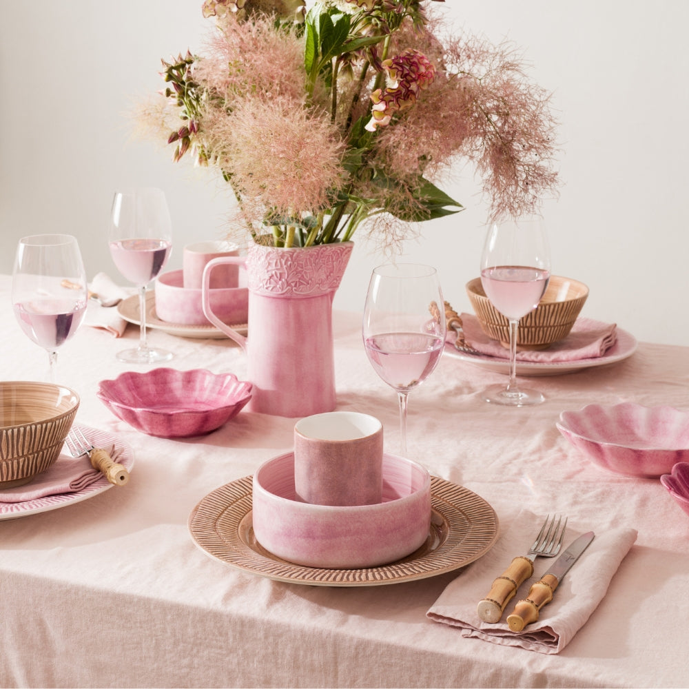 Dining table set with pink ceramic dishes, glasses, and a vase of flowers.