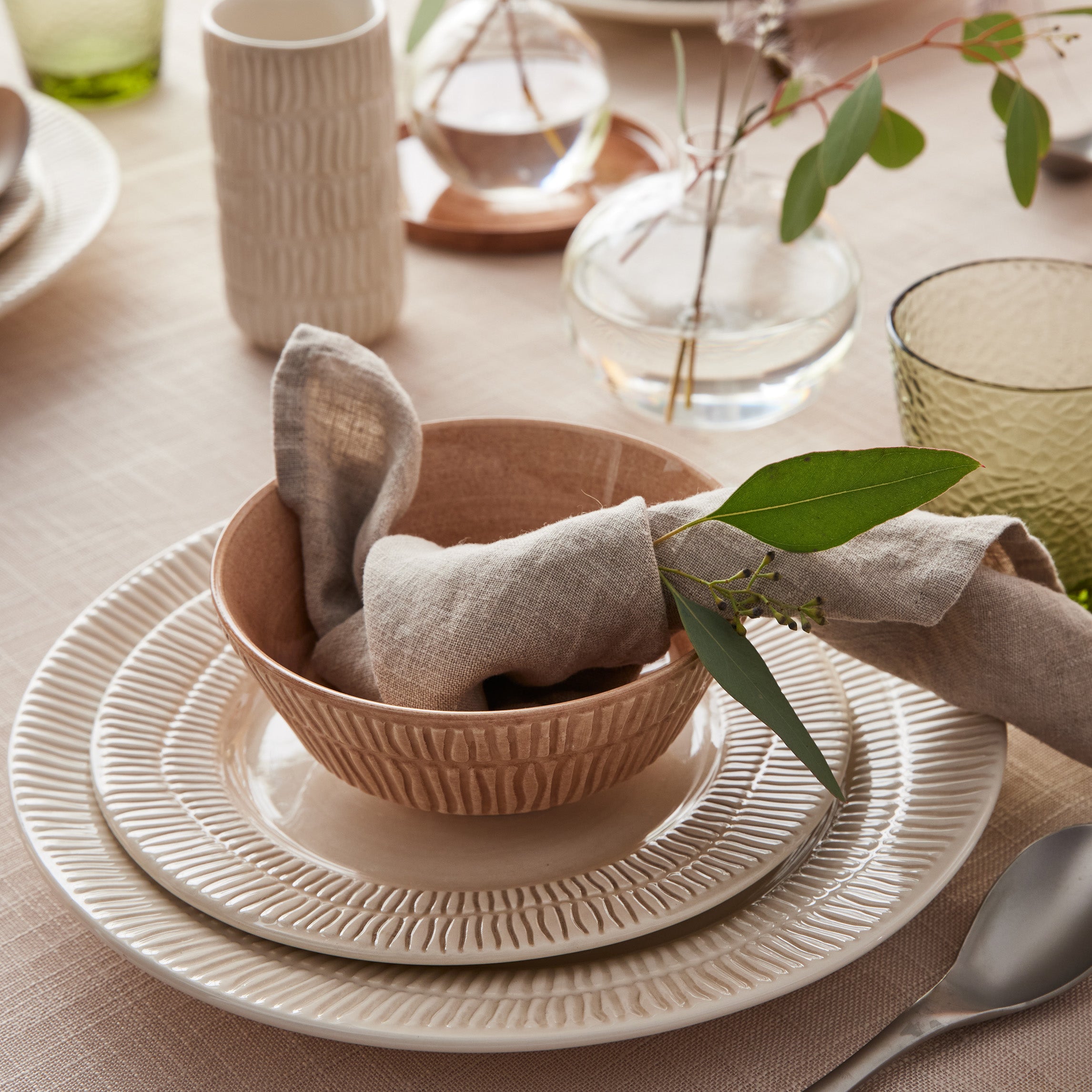 Dining table setting with a bowl, plates, and napkins on a beige tablecloth.