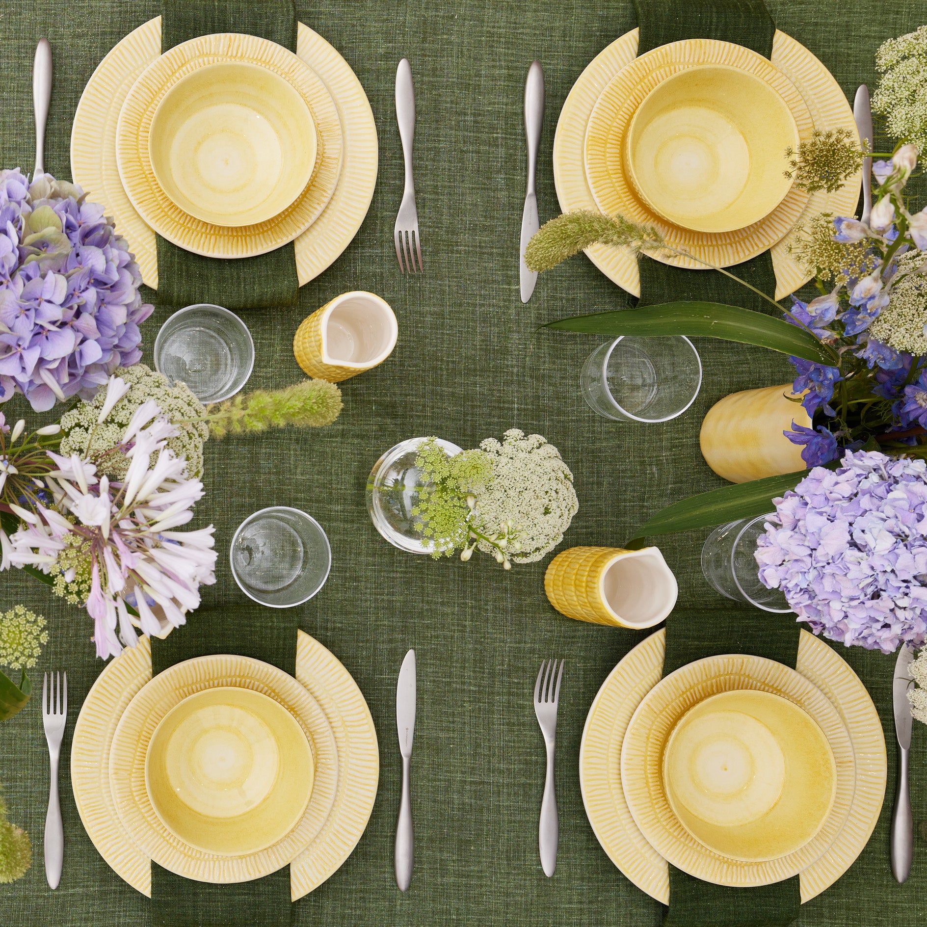 Elegant table setting with yellow plates, silverware, and purple flowers on a green tablecloth.