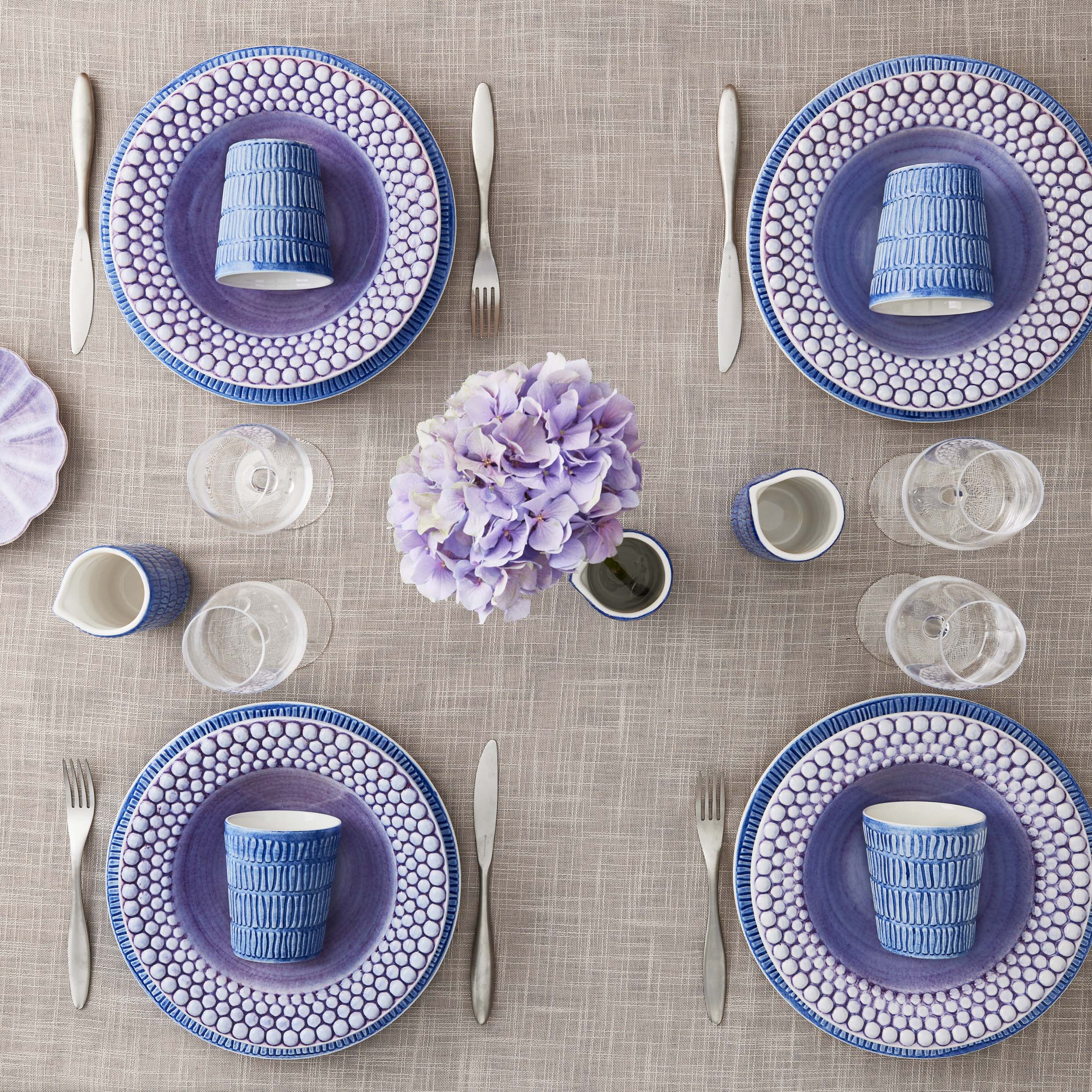 Table setting with blue and white ceramic plates, cups, and cutlery on a textured tablecloth.