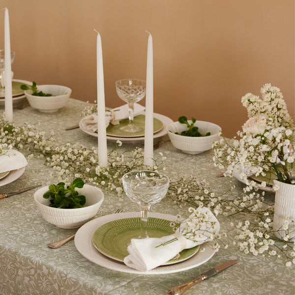 Elegant table setting with green plates, white candles, and floral decorations on a beige background.