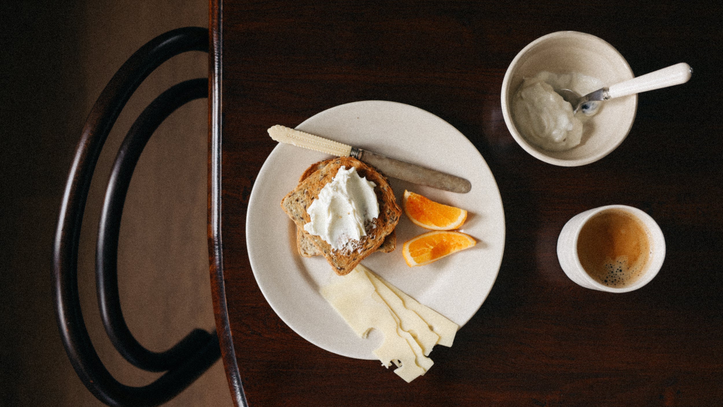 Breakfast setting with toast, cream, orange slices, and a cup on a wooden table.