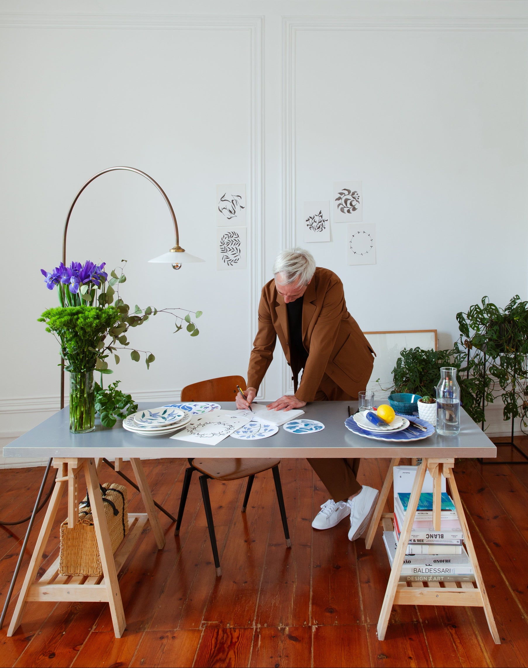 Person in a brown coat standing at a table with decor items in a room with white walls and wooden floor.